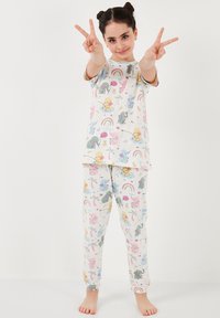 Puuvillainen pyjamapuku, jossa on valkoinen tausta ja värikkäitä eläin- ja sateenkaari-kuvioita. Lyhythihainen paita ja pitkät housut, joissa on joustavat nilkkakappaleet.