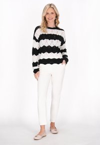 Maglione a maglia bianco e nero con motivo a scallop, abbinato a pantaloni bianchi slim e ballerine in tonalità chiare.