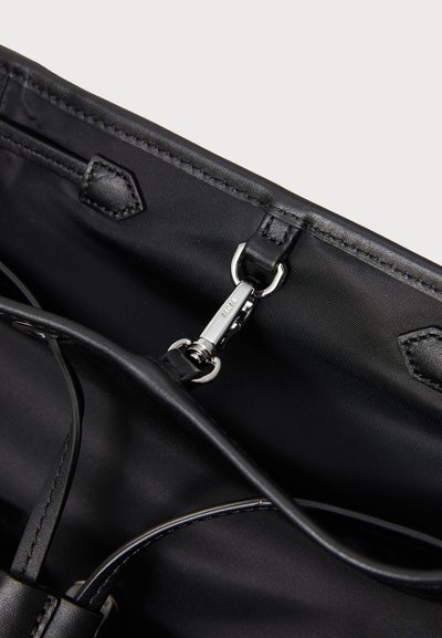 Interior de un bolso de tela negra y cuero con un cierre de metal plateado y detalles de lazo de cuero en el borde superior.