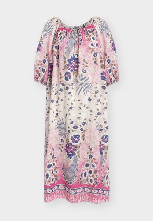 Frau trägt ein langes, lockeres rosa-weißes Blumenkleid mit dreiviertel Ärmeln, hält eine weiße Clutch und trägt beige Riemchenabsätze.