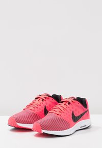 Baskets de course en mesh rose avec des accents noirs, présentant un revêtement texturé et une semelle blanche. Les lacets sont assortis en rose. Logo Nike sur le côté.