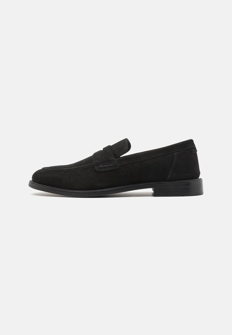 Mocassins en daim noir avec une texture lisse, un bout rond et une lanière décorative. Ils présentent un talon bas et solide ainsi que des détails de couture subtils.