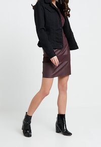 Veste en denim noire avec un col texturé, robe en cuir bordeaux et bottines noires brillantes avec un large talon. Tenue urbaine moderne.