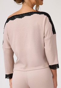 Różowy sweter z prążkowanej dzianiny w stylu off-the-shoulder. Posiada czarną koronkową lamówkę wzdłuż dekoltu i mankietów. Rękawy trzyczwartowe i luźny krój.