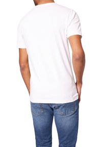 Weißes Baumwoll-T-Shirt mit Rundhalsausschnitt, kurzen Ärmeln und einem schlichten Rücken. Kombiniert mit blauen Denim-Jeans, die leicht ausgebleicht sind.