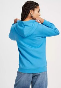 Niebieska bluza z kapturem wykonana z miękkiego materiału, charakteryzująca się luźnym krojem, ściśniętymi mankietami i kapturem ze sznurkiem. Podszewka dla większego komfortu.