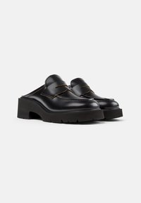 Mule in pelle nera con punta arrotondata, cuciture a contrasto e una suola piatta spessa e testurizzata. Design slip-on senza retro.