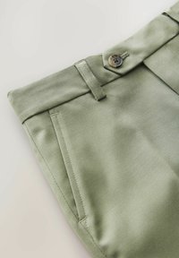 Light green chino pants with a smooth texture, featuring a button closure, belt loops, and side pockets. Simple, tailored design.