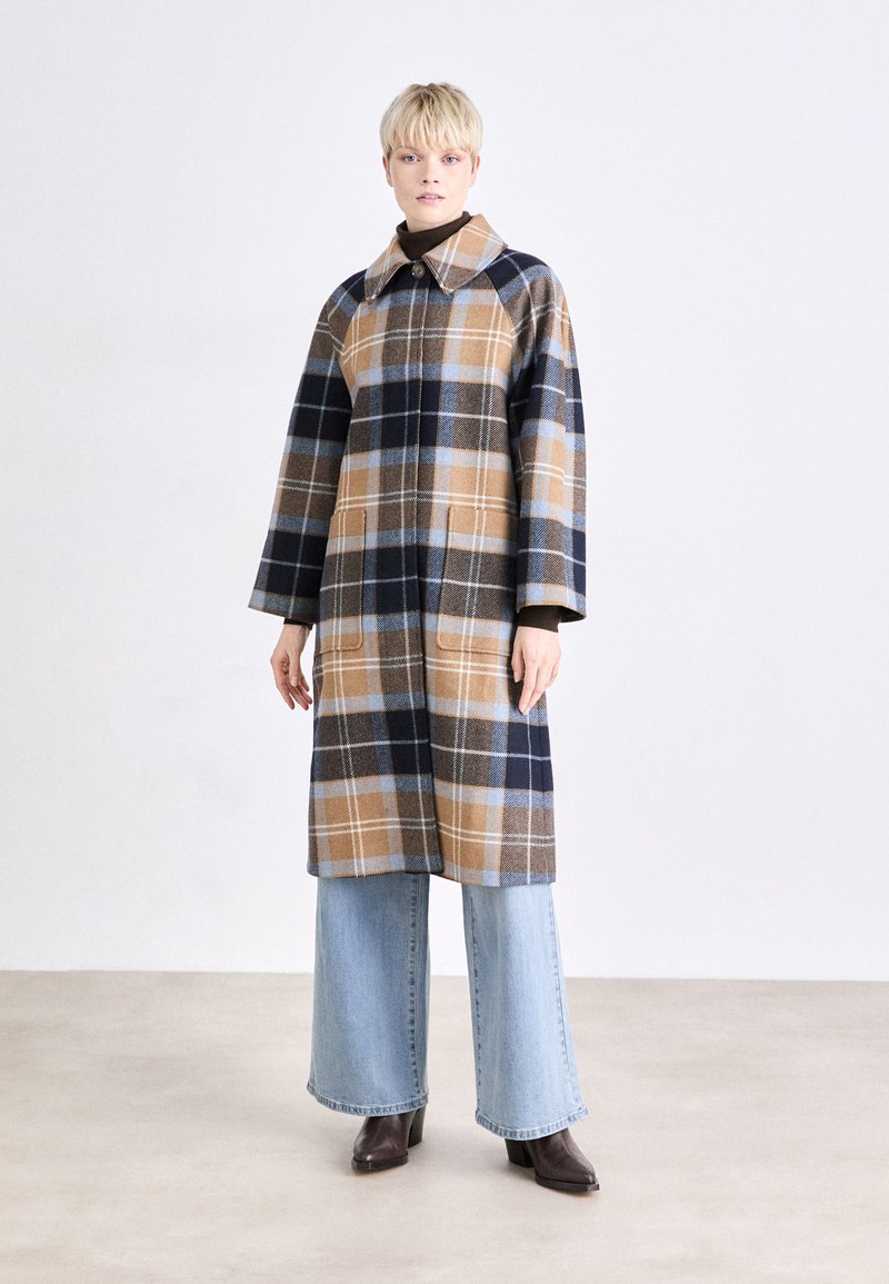 Plaid coat in brown, navy, and light blue tones, featuring a large collar, long sleeves, and two front pockets. Worn over wide-leg jeans.