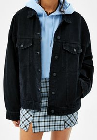 Svart denimjacka med knäppningar, två bröstfickor, sliten detalj; lager över en ljusblå hoodie och matchad med en rutig kort kjol.