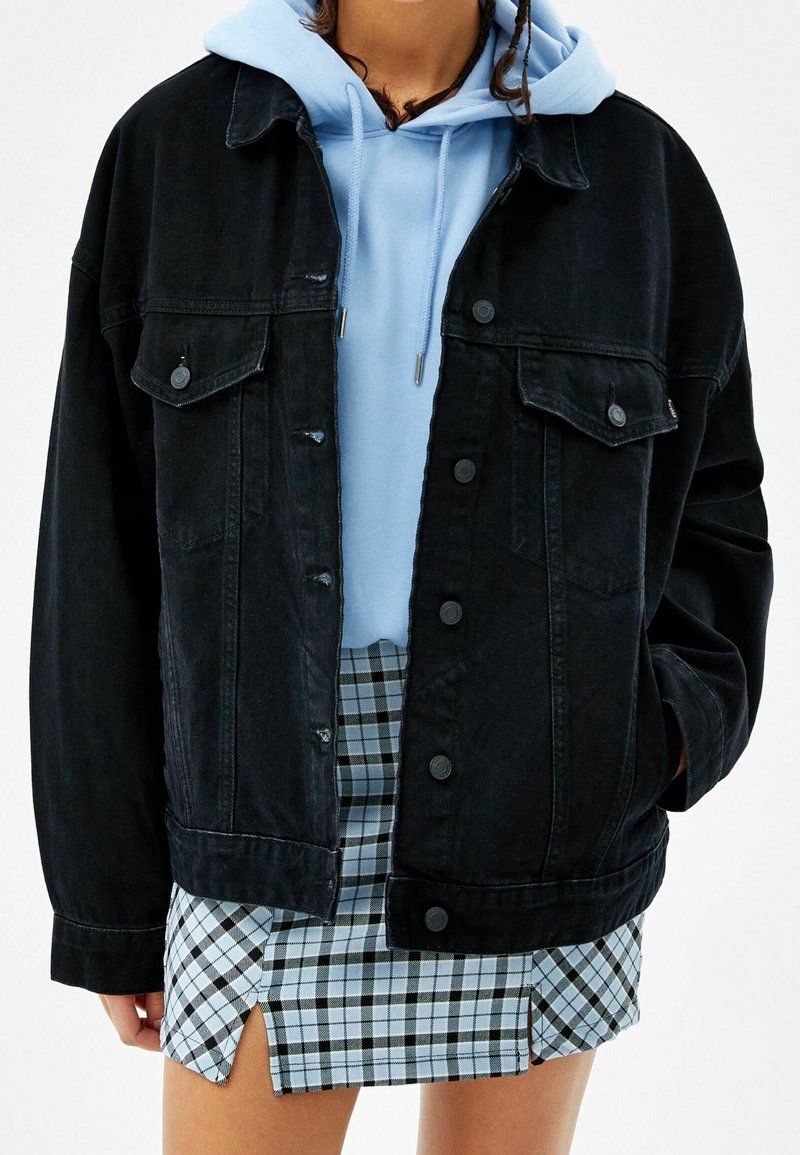 Svart denimjacka med knäppningar, två bröstfickor, sliten detalj; lager över en ljusblå hoodie och matchad med en rutig kort kjol.