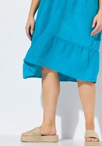 Türkises Leinenkleid mit einem Rüschensaum, kombiniert mit beigen, gewebten Plattform-Sandalen mit einem Mehrfarbigen Streifenmuster und flacher Sohle.