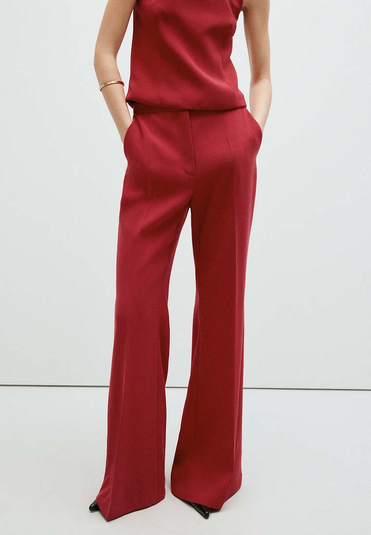 Personne portant un pantalon rouge taille haute à jambes larges et un haut sans manches assorti, avec les mains dans les poches et des chaussures noires pointues visibles.