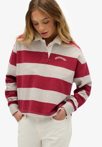 Maglia polo a maniche lunghe a righe rosse e grigie con colletto bianco e logo ricamato. Presenta una vestibilità comoda e dettagli di cuciture visibili.