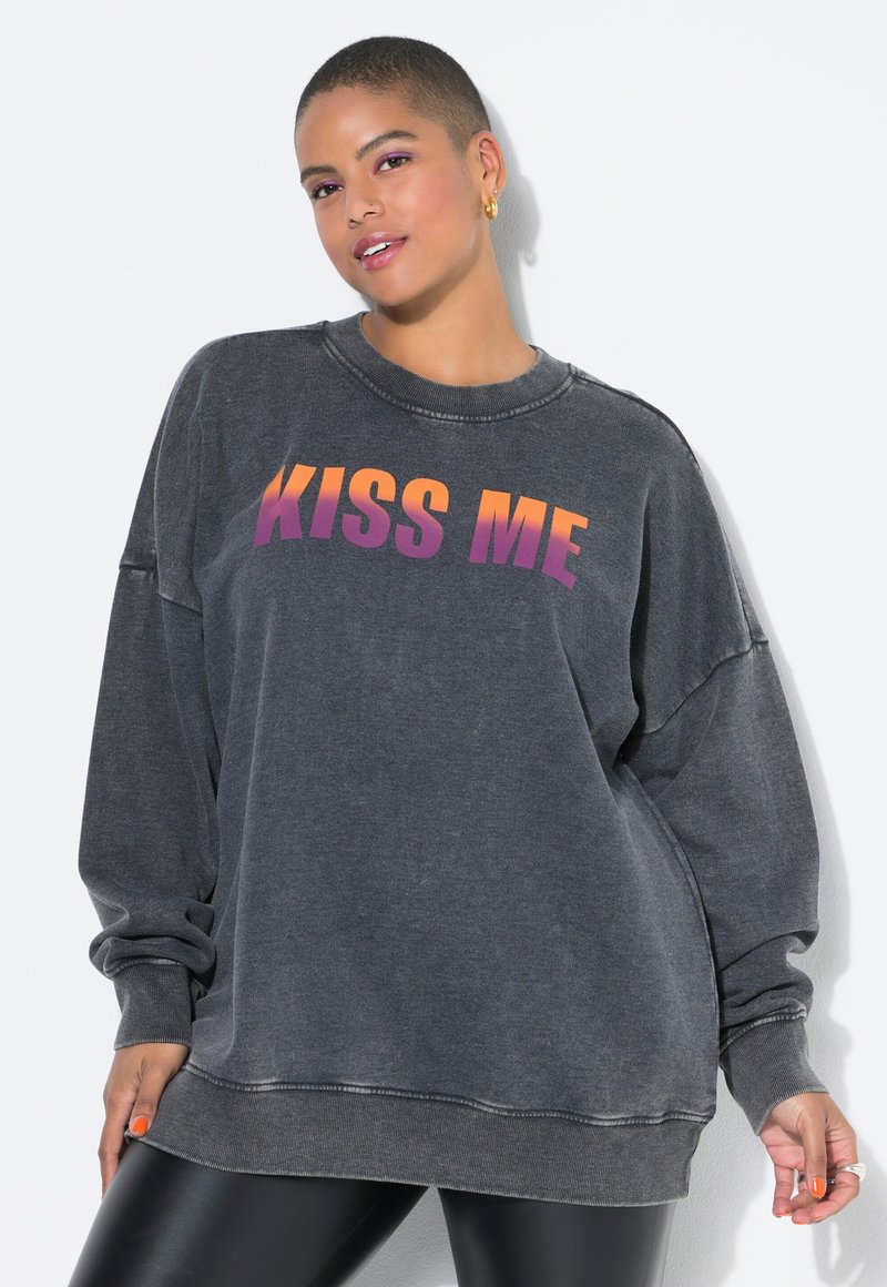 Grijze oversized sweatshirt met "KISS ME" in een verloop van oranje naar paarse letters. Heeft ribgebreide mouwen en een relaxte pasvorm. Soepele textuur.