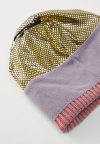 Gorro de malha dourada com fleece roxo, apresentando uma faixa listrada laranja. A sobreposição de malha tem um acabamento cintilante, contrastando com o tecido suave abaixo.
