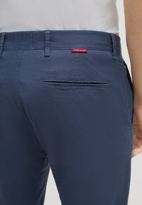 Pantaloni in tessuto blu navy con tasca posteriore, dotati di un'etichetta rossa "JOOP! JEANS" sopra il girovita. Vestibilità su misura con passanti per cintura.