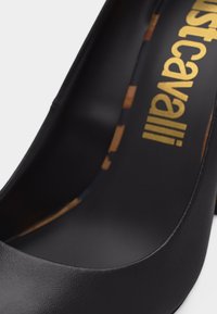 Κοντινό πλάνο της εσωτερικής περιοχής της φτέρνας ενός μαύρου δερμάτινου τακουνιού με γράμματα του ονόματος της μάρκας σε χρυσαφί χρώμα.