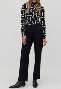 Långärmad topp med ett svart och vitt vågmönster, tillsammans med skräddarsydda svarta byxor och spetsiga svarta ankboots.