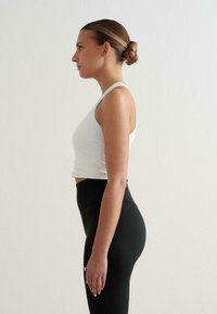 Fehér rövidtop, melyet magas derekú fekete leggings-szel párosítanak. Sima anyag, testhezálló forma, látható minták vagy díszítések nélkül. Egyszerű sziluett.