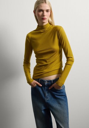 Langärmliges, senfgelbes Oberteil mit hohem Kragen; taillierter Schnitt. Kombiniert mit hellblauen, locker geschnittenen Denim-Jeans. Schlichter, strukturierter Stoff.