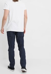 Marinrandiga byxor med avslappnad passform, tillverkade av ett mjukt tyg. Kombineras med en enkel vit t-shirt och svarta sneakers.