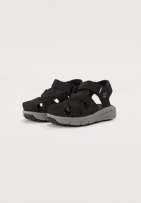 Sandalias negras con diseño abierto, correas ajustables y suela de goma gris. Presentan cortes para una mejor transpirabilidad y material superior texturizado.