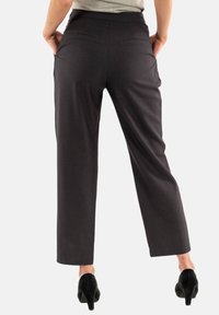 Pantalones de tiro alto en gris oscuro con un corte ajustado, dos bolsillos traseros y una textura suave, combinados con zapatos de tacón negros.