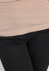Top aderente rosa chiaro con texture a coste, indossato sopra jeans neri caratterizzati da una superficie liscia e leggere sfumature nella parte anteriore.