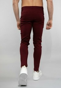 Pantalons slim-fit bordeaux avec une texture lisse, dotés d'une taille standard et de poches arrière, associés à des baskets blanches.