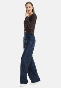 Dark brown long-sleeve top paired with navy blue, loose-fitting pants featuring side pockets and a subtle logo accent. White footwear.