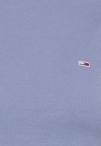 Ljusblå ribbad t-shirt med en liten broderad logotyp i rött, vitt och blått. Tillverkad av mjukt, elastiskt tyg.