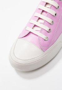 Rosa lädersneakers med vit gummikåpa, utrustad med vita skosnören och metallöglor. Slät textur, enkel design med sömnadsdetaljer.