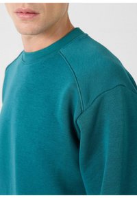 Teal sweatshirt met een ronde hals, raglanmouwen en een zachte textuur. De stof lijkt glad met een subtiele glans.