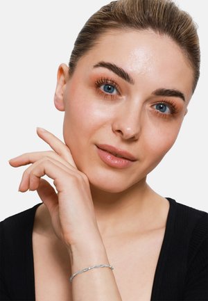Bracciale d'argento intrecciato su un polso, pelle liscia, top nero a contrasto, trucco naturale con toni neutri e ombretto delicato.