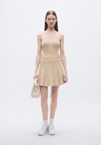 Top corto sin mangas beige acanalado y minifalda plisada, combinados con zapatillas blancas y un pequeño bolso crema. Tela suave con textura sutil.