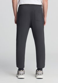 Ciemnoszare dresy o tapered design, z tylną kieszenią i elastycznym pasem, zestawione z jasnymi sneakersami.