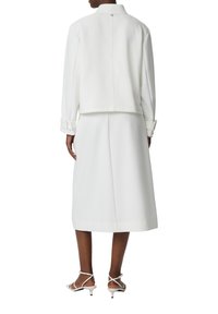 White coat with a high neck and button closure, paired with a matching midi skirt. Features structured sleeves and a smooth texture.