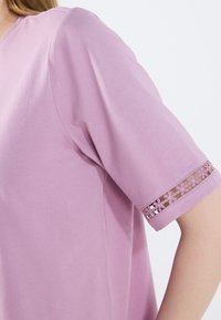 Lila kortärmad topp i mjukt tyg med V-ringning. Har en delikat blommig spetskant vid ärmsluten. Slät textur.