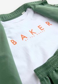 Bílý tričko s oranžovým nápisem "BAKER BY TED BAKER" spárované se zelenou lehkou bundou s texturovanou látkou.