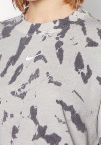 Sudadera gris con patrón de teñido anudado negro, cuello redondo y pequeño logo blanco de Nike. La tela parece suave con un acabado texturizado.