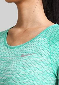 Grünes Sportoberteil mit strukturiertem Muster, Rundhalsausschnitt und silbernem Nike-Logo auf der Brust. Weicher Stoff, figurschmeichelnde Passform.