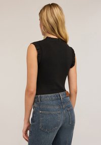 Top senza maniche a coste nere con dettagli arricciati sulle spalle, abbinato a jeans in denim blu a vita alta con tasche posteriori e una etichetta in pelle.