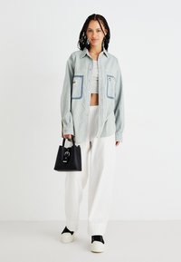 Camicia azzurra a righe sottili con due tasche frontali, indossata sopra un crop top grigio. Abbinata a pantaloni bianchi a gamba larga e scarpe nere con plateau. Borsa nera.