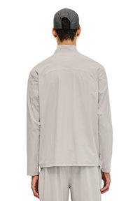 Hellgraues Langarmshirt mit hohem Kragen und Rückensattel-Detail, aus glattem Stoff, kombiniert mit passenden Hosen.