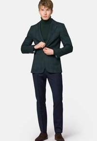 Zielona kratkowana marynarka na ciemnym golfie, zestawiona z granatowymi spodniami. Brązowe buty. Marynarka posiada klapy z ząbkami i akcenty przy guzikach.