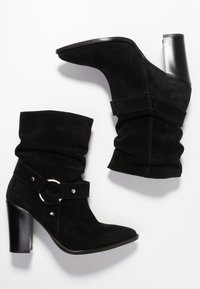 Musta mokkanahkasaapikkaat, joissa on rento muotoilu, korkea lohkarekorko ja leveä hihna, jossa on pyöreä hopeinen metallikoriste.