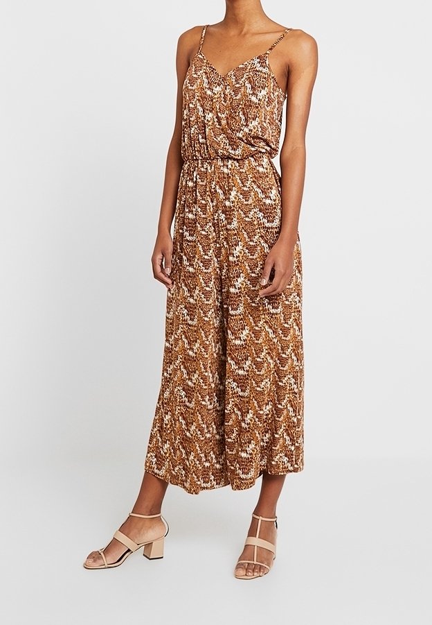 Bruin gemusterde jumpsuit met een ontspannen pasvorm, dunne bandjes en een elastische tailleband. Gecombineerd met beige blockhak-sandalen.