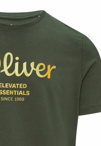 Dunkelgrünes T-Shirt mit kurzen Ärmeln und goldenem Text "Oliver", "Elevated Essentials" und "Seit 1969" auf der Vorderseite.