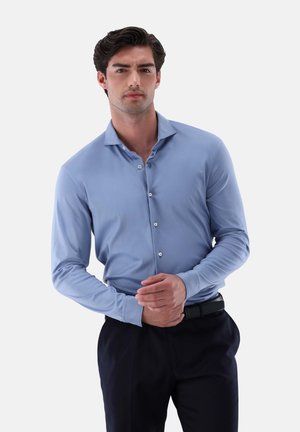 Camicia a maniche lunghe azzurro chiaro con colletto button-down, caratterizzata da bottoni bianchi, texture liscia, abbinata a pantaloni scuri e una cintura nera.